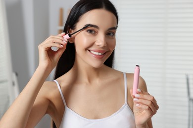 Beautiful young woman applying mascara with brush indoors