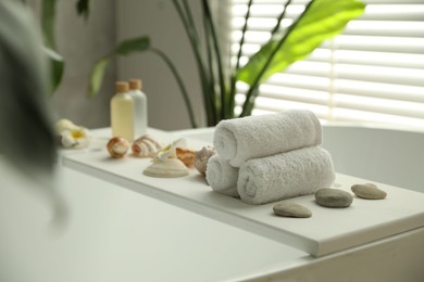 Bath tray with spa products and towels on tub in bathroom