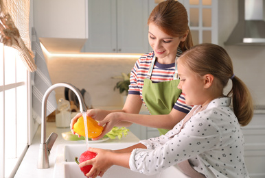 Photo of Mother and daughter washing vegetables in kitchen