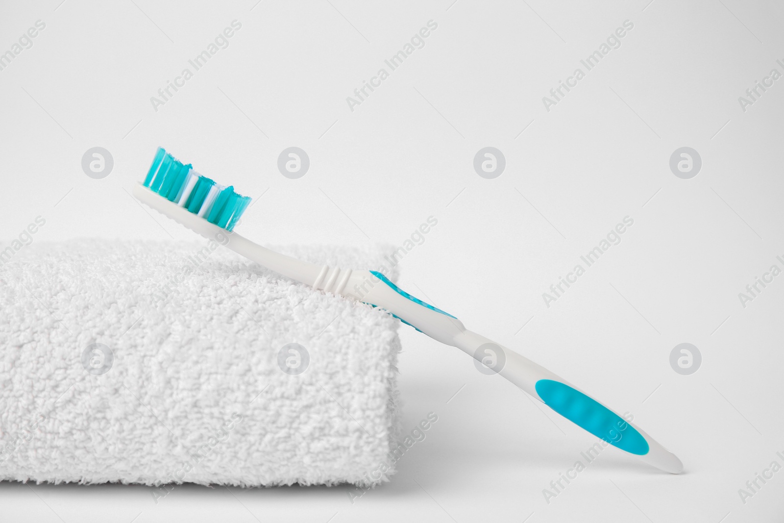 Photo of Light blue toothbrush and terry towel on white background