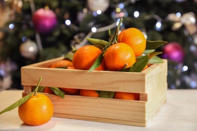 Photo of Wooden crate with ripe tangerines and Christmas tree on background