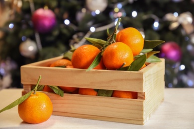 Wooden crate with ripe tangerines and Christmas tree on background