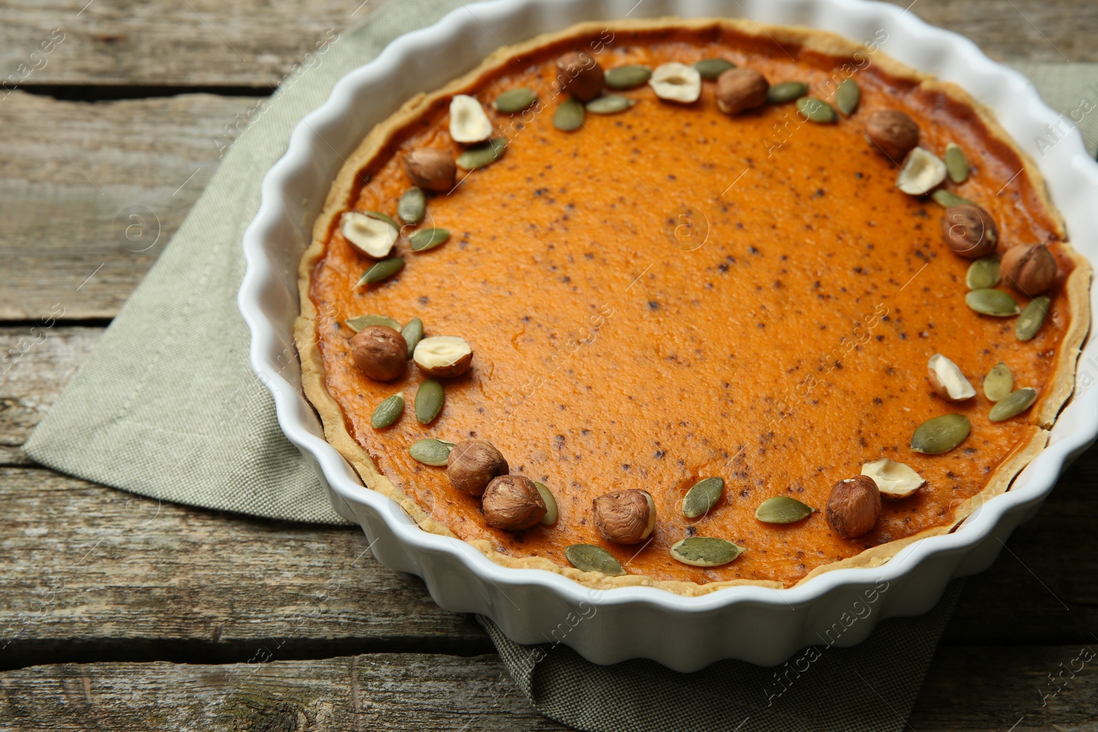 Photo of Delicious pumpkin pie with seeds and hazelnuts on wooden table, closeup