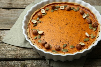 Photo of Delicious pumpkin pie with seeds and hazelnuts on wooden table, closeup
