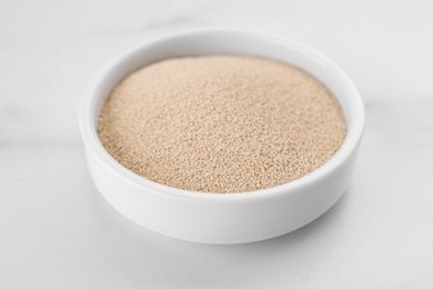 Photo of Bowl of active dry yeast on white marble table, closeup