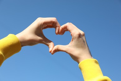 Photo of Woman showing heart against blue sky outdoors on sunny day, closeup of hands