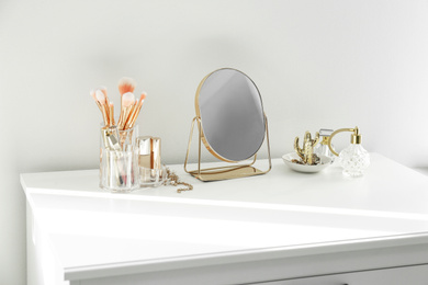 Photo of Small mirror and makeup products on white dressing table indoors