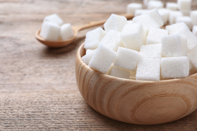 Refined sugar in bowl on wooden table, closeup