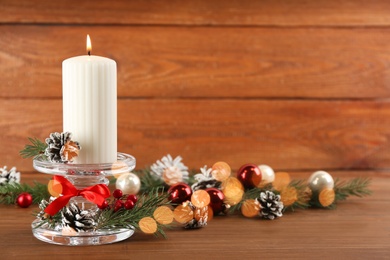 Glass candlestick with burning candle and Christmas decor on wooden table. Space for text