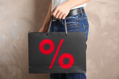 Image of Man holding paper shopping bag with percent sign near beige wall, closeup. Discount concept