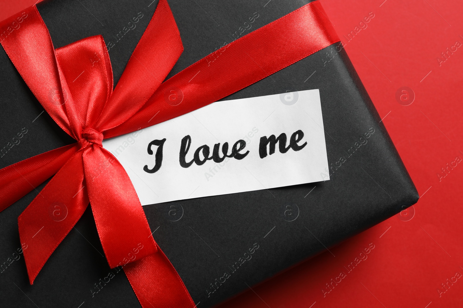 Photo of Tag with handwritten phrase I Love Me and gift box on red background, top view