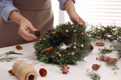 Photo of Florist making beautiful Christmas wreath at white wooden table indoors, closeup