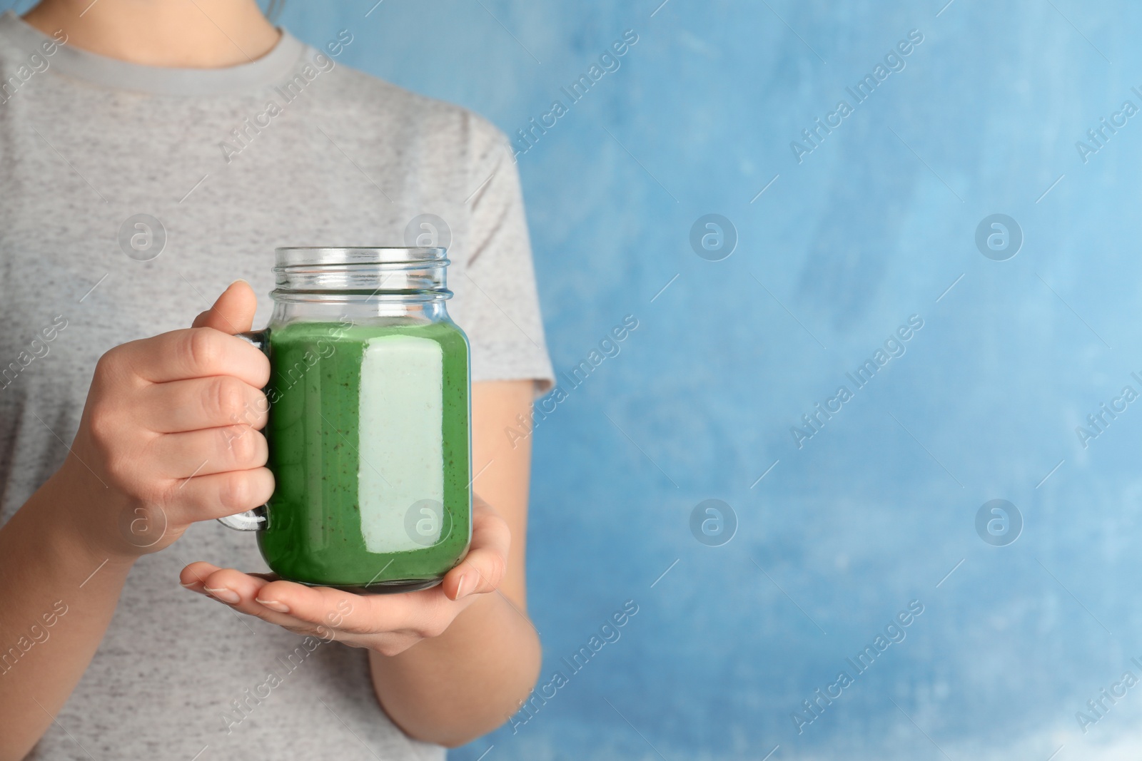 Photo of Woman holding mason jar of spirulina smoothie on color background, closeup. Space for text