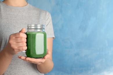 Photo of Woman holding mason jar of spirulina smoothie on color background, closeup. Space for text