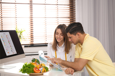 Photo of Young nutritionist consulting patient at table in clinic