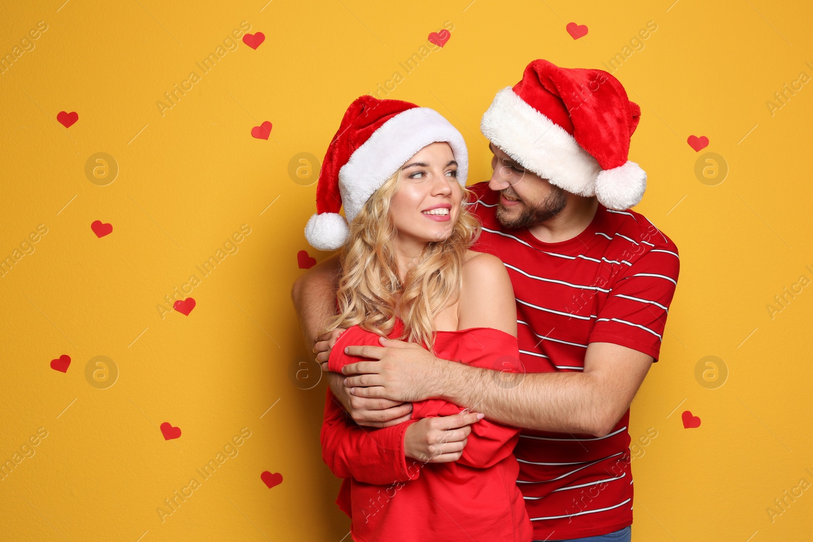 Photo of Young couple in Santa hats on color background. Christmas celebration