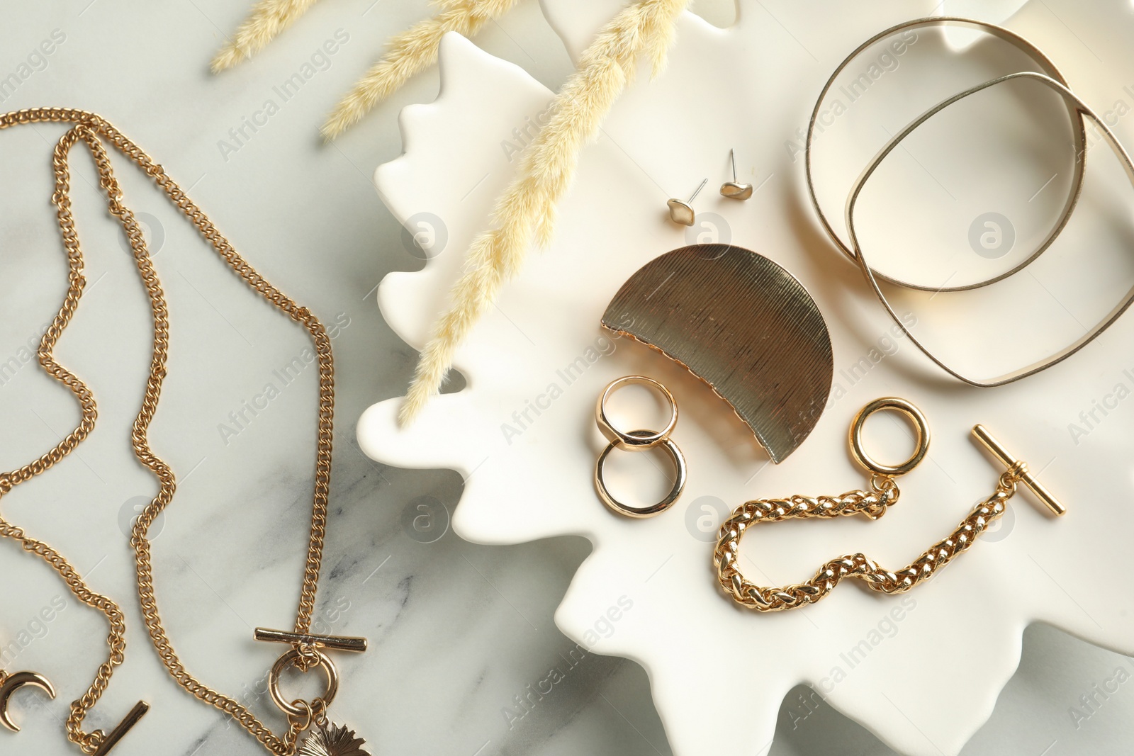 Photo of Different elegant bijouterie and plate on white marble table, flat lay