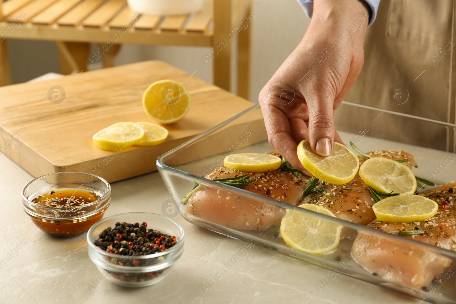 Photo of Woman cooking chicken breasts with lemon at grey marble table, closeup