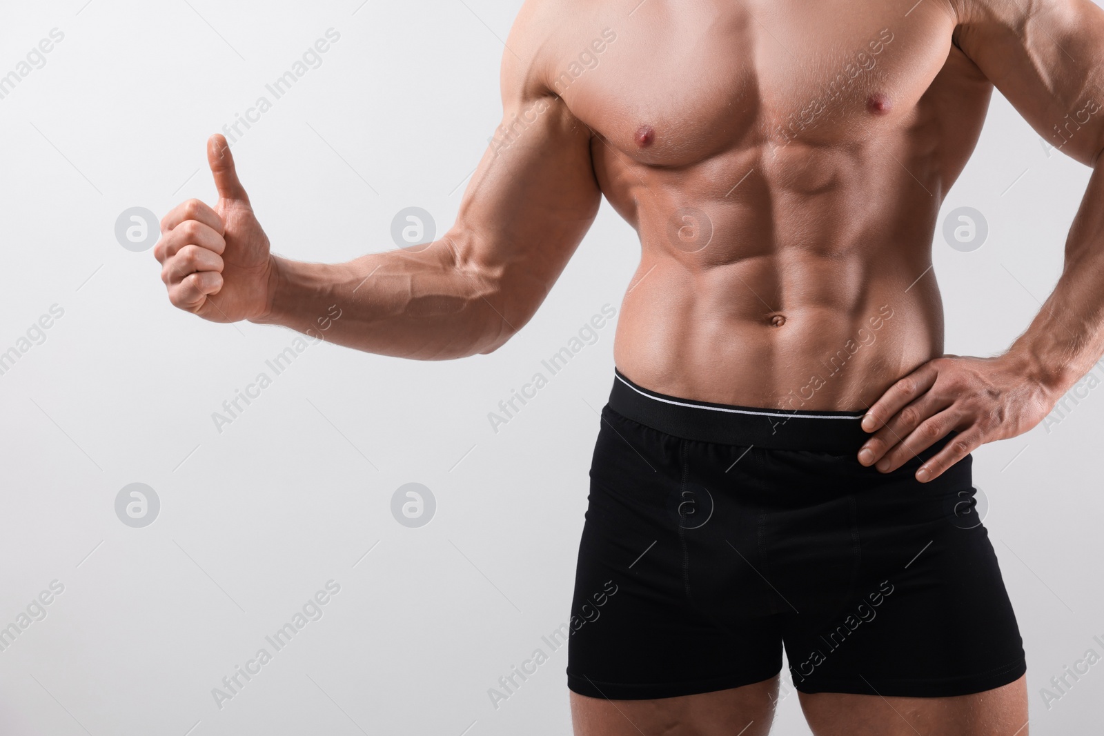 Photo of Young man is stylish black underwear showing thumb up on light grey background, closeup