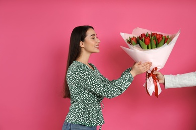 Happy woman receiving red tulip bouquet from man on pink background. 8th of March celebration