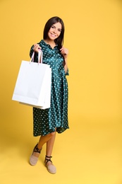 Photo of Full length portrait of young woman with paper bags on yellow background