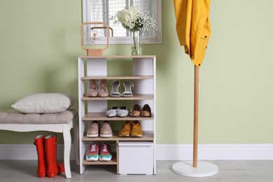 Wooden shelving unit with shoes and different accessories near green wall in hall. Storage idea