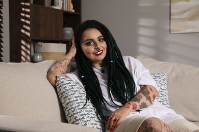 Beautiful young woman with tattoos on body, nose piercing and dreadlocks at home