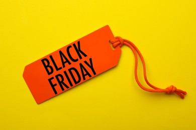 Image of Orange tag with phrase BLACK FRIDAY on yellow background, top view