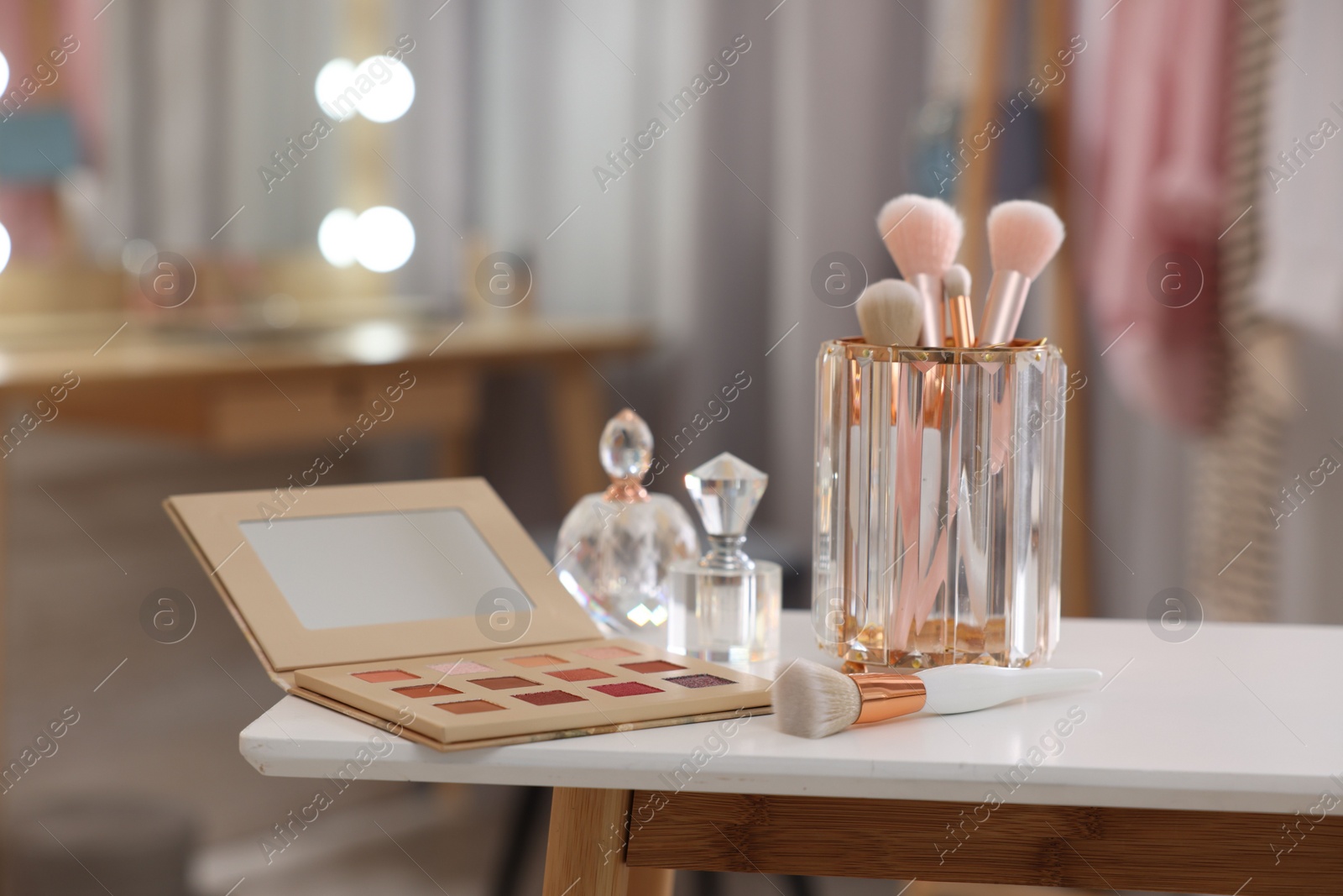 Photo of Set of brushes, eyeshadow palette and perfumes on white table in makeup room