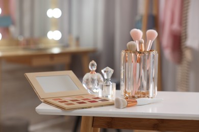 Photo of Set of brushes, eyeshadow palette and perfumes on white table in makeup room