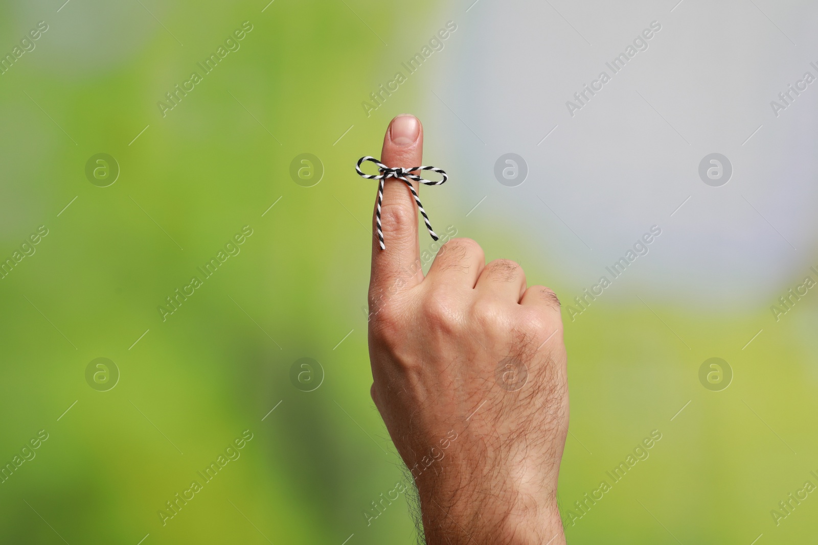 Photo of Man showing index finger with tied bow as reminder on green blurred background, closeup