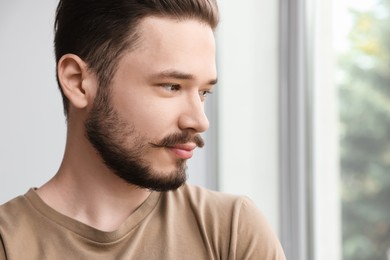 Handsome man near window indoors, closeup. Space for text