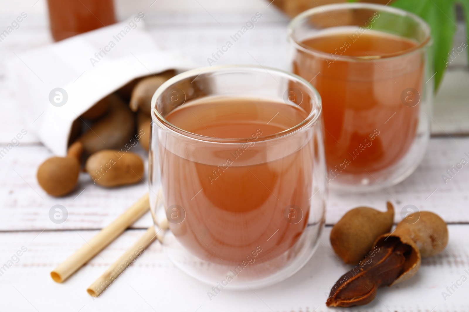 Photo of Tamarind juice and fresh fruits on white wooden table, closeup