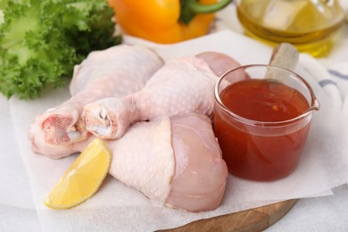 Fresh marinade, raw chicken drumsticks and lemon wedge on light table, closeup