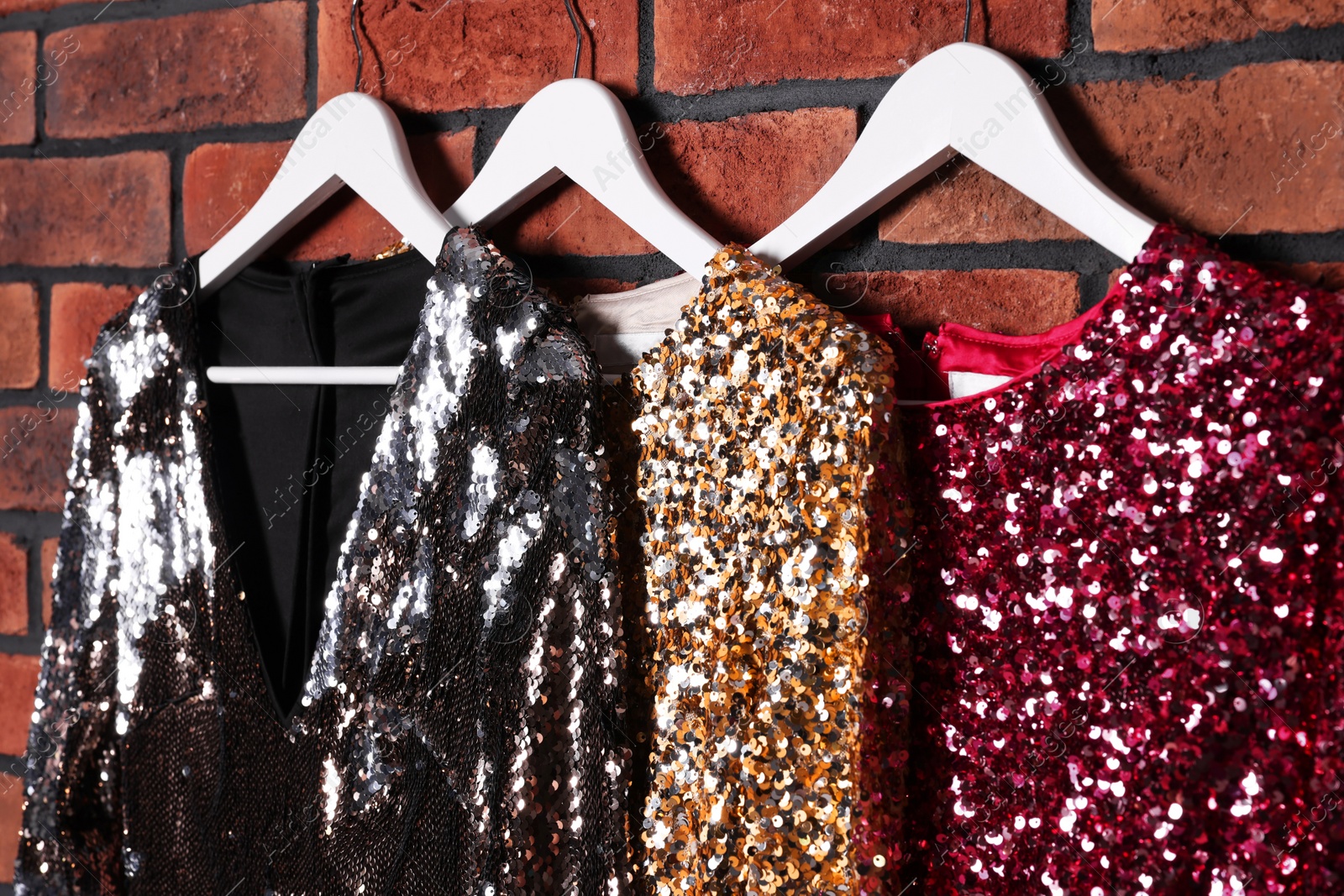 Photo of Different shiny beautiful women's party dresses on hangers near brick wall. Stylish trendy clothes for high school prom