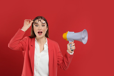 Photo of Emotional young woman with megaphone on red background