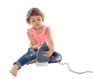 Little girl playing with iron on white background. Danger at home