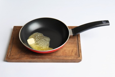 Photo of Frying pan with melting butter on board against white background