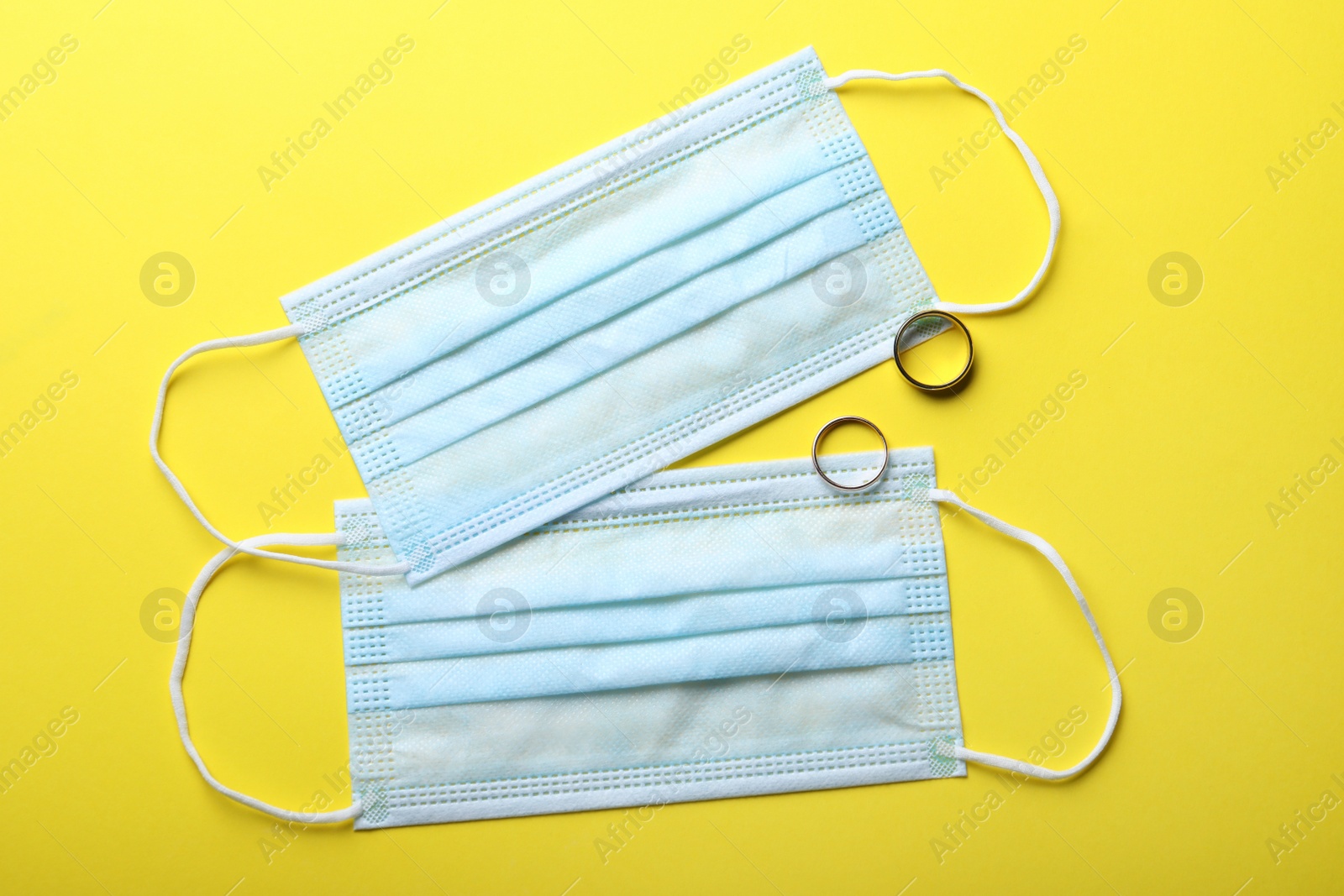 Photo of Protective masks and wedding rings on yellow background, flat lay. Divorce during coronavirus quarantine