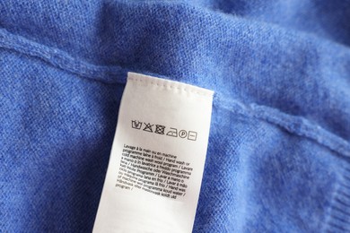 Photo of Clothing label in different languages on blue garment, top view