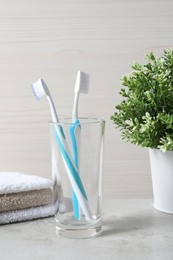 Plastic toothbrushes in glass holder and towels on light grey table
