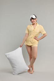 Photo of Happy woman in pyjama and sleep mask holding pillow on grey background