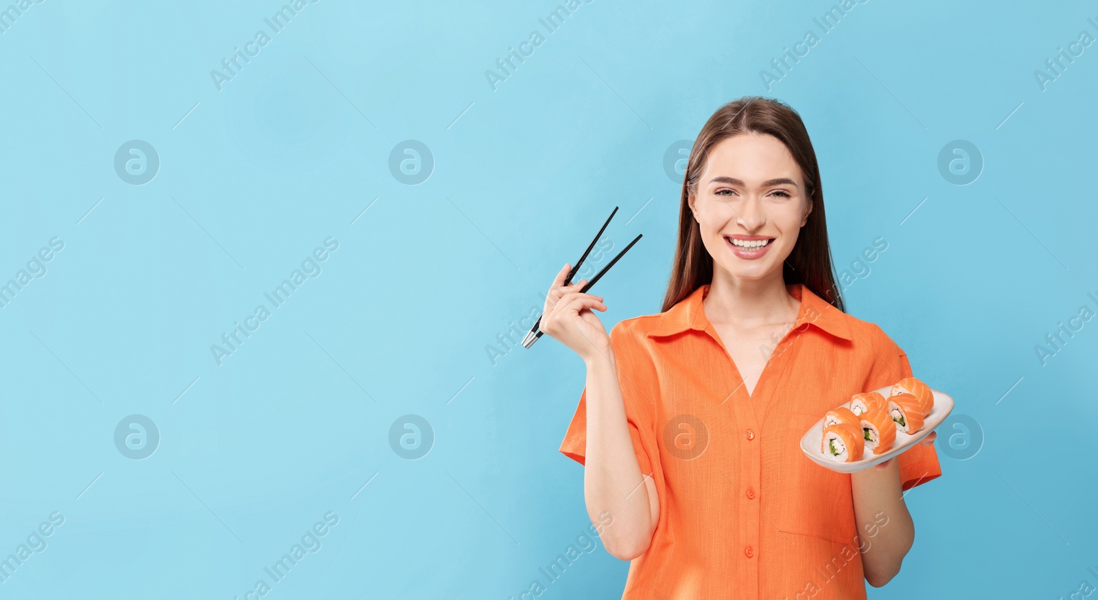 Photo of Happy young woman with plate of sushi rolls and chopsticks on light blue background. Space for text