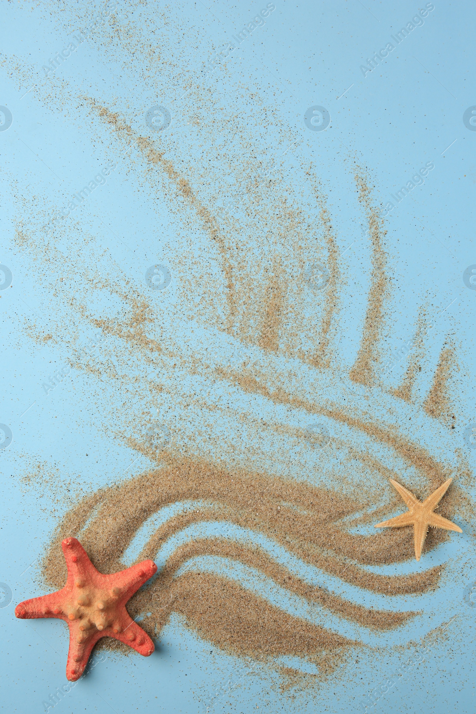 Photo of Beautiful sea stars and sand on light blue background, flat lay. Space for text