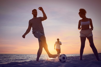 Friends playing football on beach at sunset