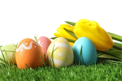 Photo of Colorful painted Easter eggs and flowers on green grass against white background