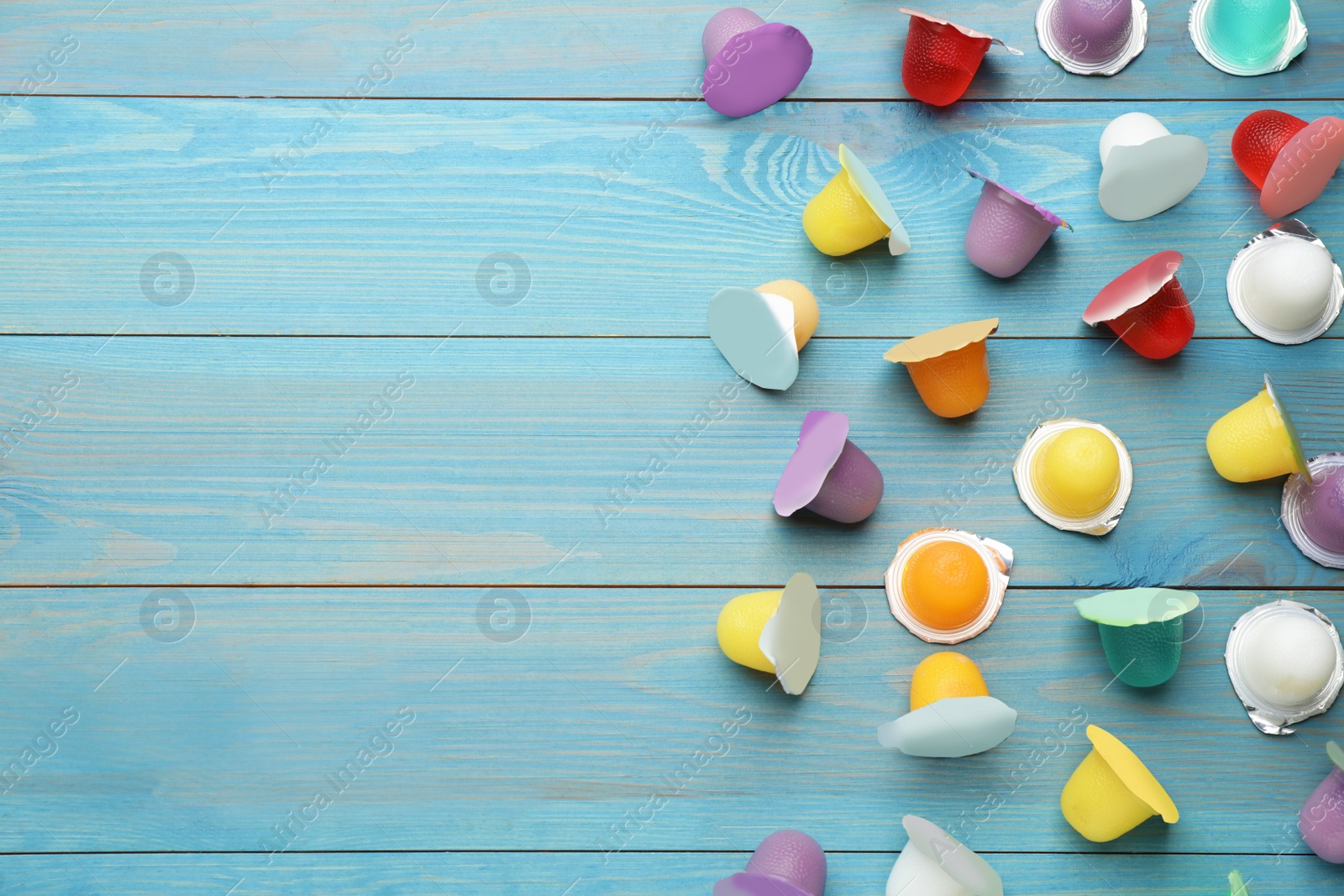 Photo of Tasty bright jelly cups on light blue wooden table, flat lay. Space for text