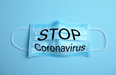 Image of Medical mask with text Stop Coronavirus on light blue background. Protective measures during pandemic