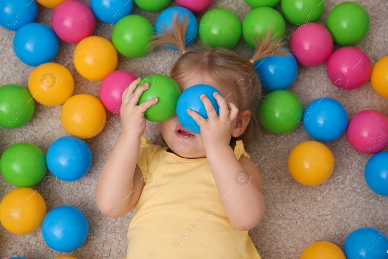 Photo of Cute little child playing with balls on floor, top view