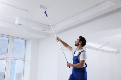 Photo of Handyman with roller painting ceiling in room